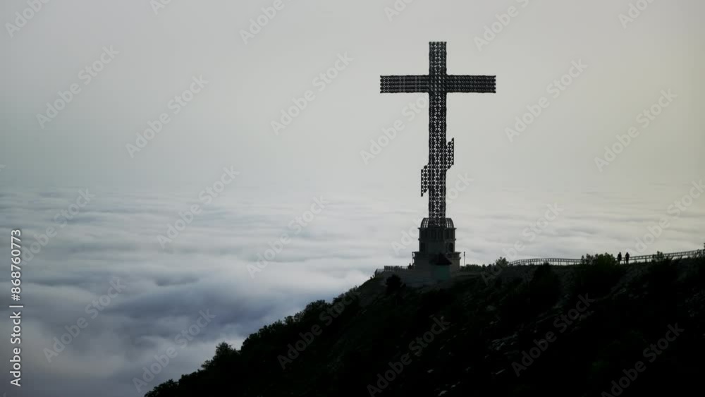 massive Christian cross towers on mountain, with clouds drifting beneath it in time-lapse. blend of religion and beauty captured in frame, where the clouds resemble a turbulent ocean at base of cross. massive Christian cross towers on mountain, with clouds drifting beneath it in time-lapse. blend of religion and beauty captured in frame, where the clouds resemble a turbulent ocean at base of cross.