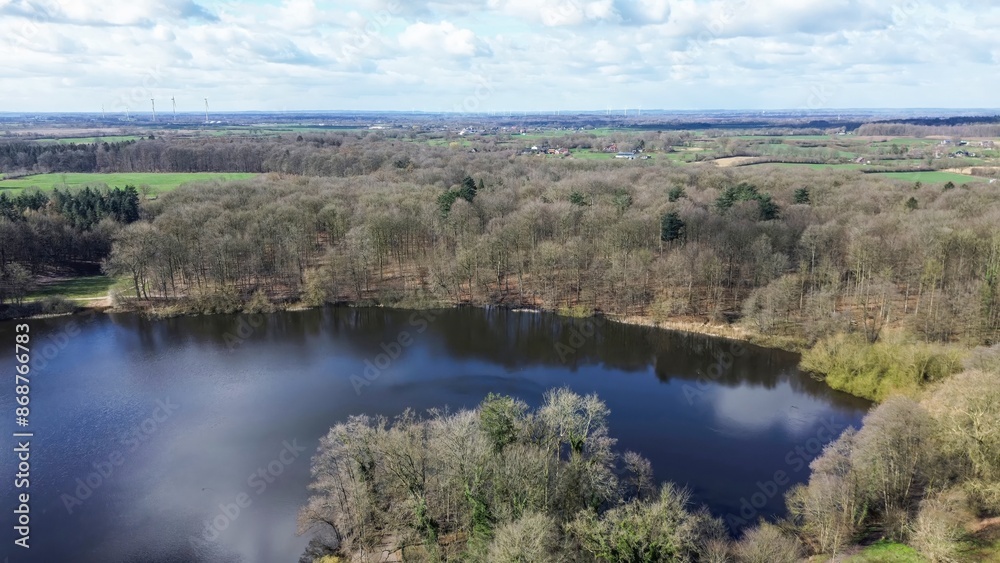 Drone view of a small lake in low sun surrounded by fields and woods.