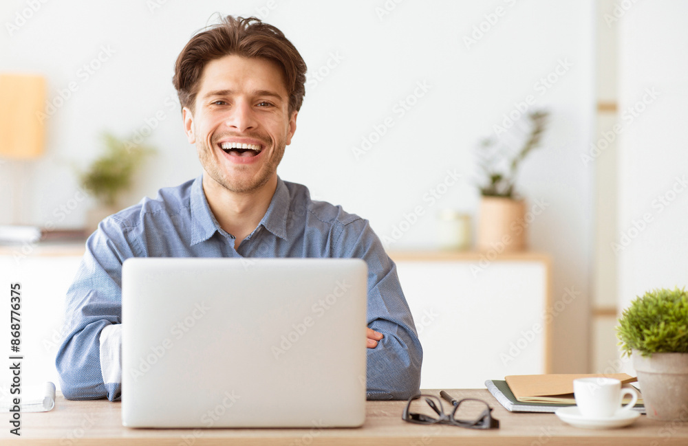 A man sits at his desk with a laptop, smiling brightly and looking at the camera. A man sits at his desk with a laptop, smiling brightly and looking at the camera.