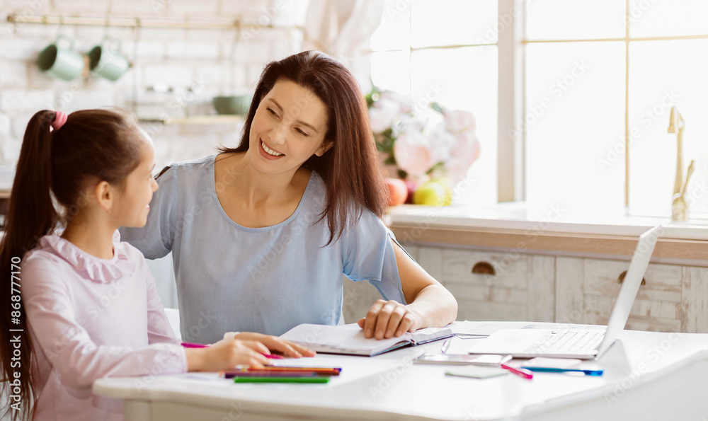 A mother and her young daughter are working together on homework at a table in their home. They are both smiling and look happy, copy space A mother and her young daughter are working together on homework at a table in their home. They are both smiling and look happy, copy space