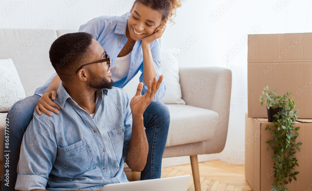 Afro Husband And Wife Using Laptop And Talking Sitting In Living Room After Moving Apartment. Copy Space Afro Husband And Wife Using Laptop And Talking Sitting In Living Room After Moving Apartment. Copy Space