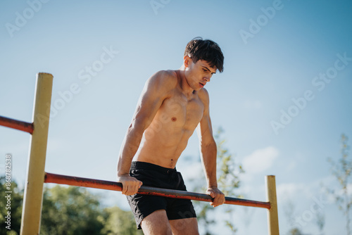 Fit young man performing a muscle-up exercise on parallel bars in a sunny outdoor setting, demonstrating strength and determination.