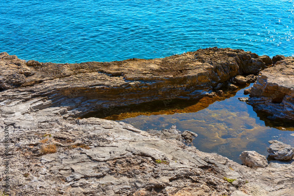 Fototapeta premium Rocky shoreline with a small body of water. Rocky coast of the island of Crete, Greece. Water is murky and the rocks are jagged