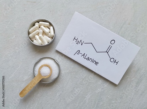 Structural chemical formula of beta-alanine with white pills and beta alanine powder. Beta alanine is an amino acid, a dietary supplement for athletic performance and muscle recovery.