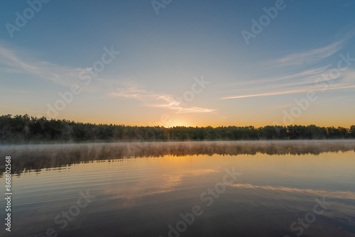 Small forest lake covered with fog at sunrise on June morning