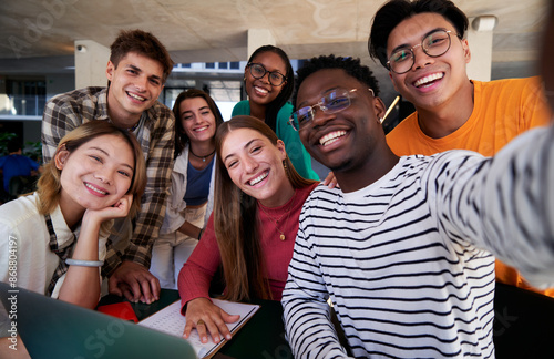 Happy selfie of a multiethnic group of student friends gathered at university studying in the cafeteria, looking at camera smiling.