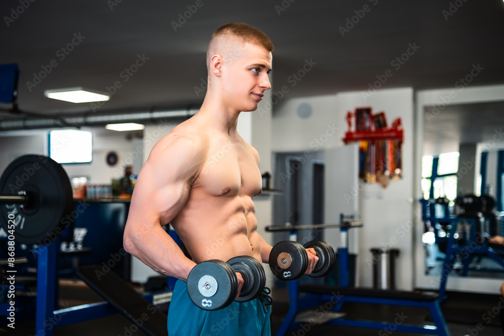 Naklejka premium A young man lifting weights in a gym. Professional bodybuilder training in the gym