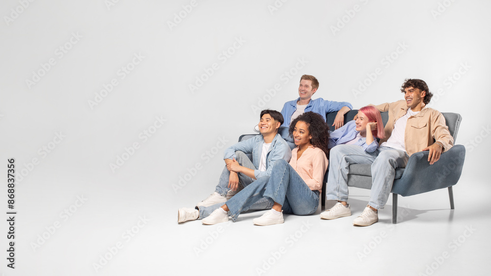 A group of five diverse friends are relaxing and enjoying each others company in a studio setting. They are sitting on a grey couch and the floor, laughing and looking happy, copy space A group of five diverse friends are relaxing and enjoying each others company in a studio setting. They are sitting on a grey couch and the floor, laughing and looking happy, copy space