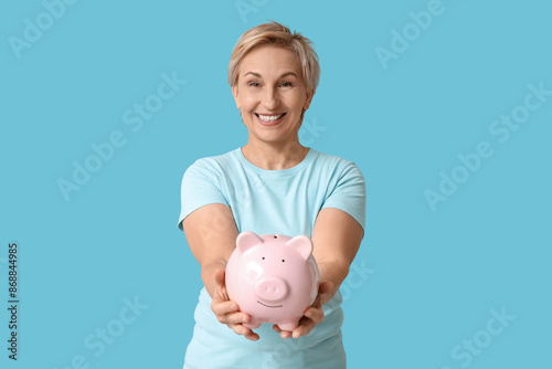 Beautiful mature woman with pink piggy bank on blue background