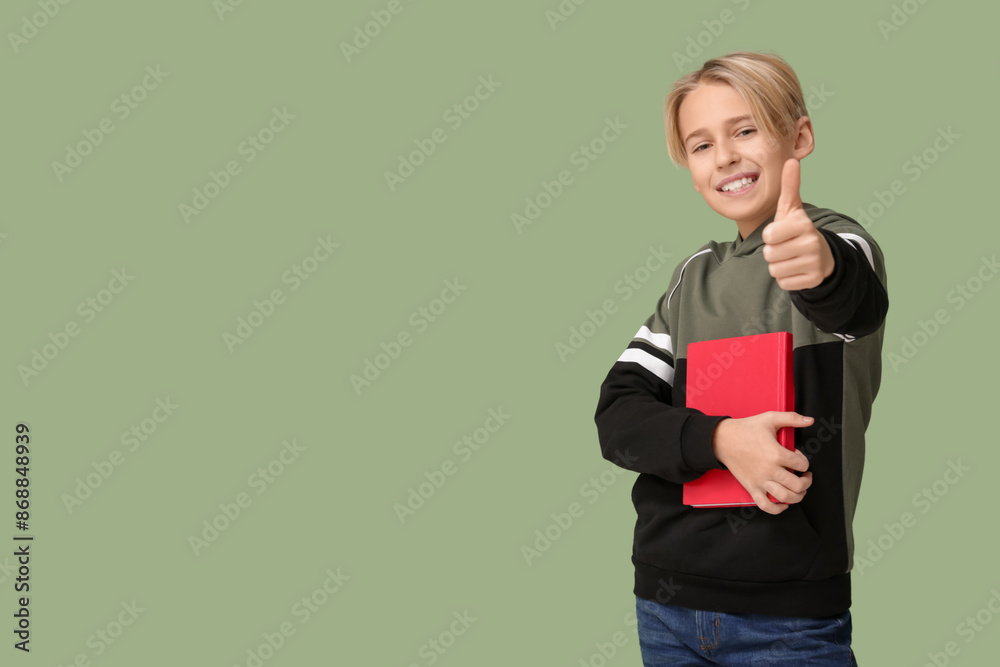 Cute little boy with book showing thumb-up gesture on green background Cute little boy with book showing thumb-up gesture on green background