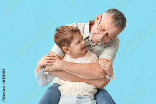 Grandfather hugging his happy cute little grandson hugging on blue background