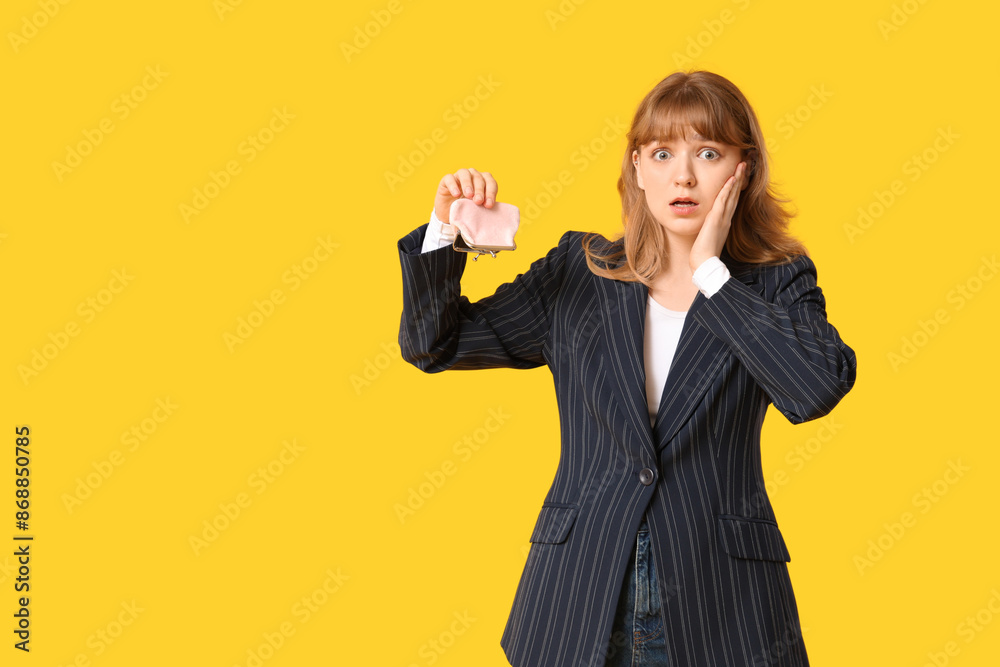 Shocked young woman holding empty purse on yellow background