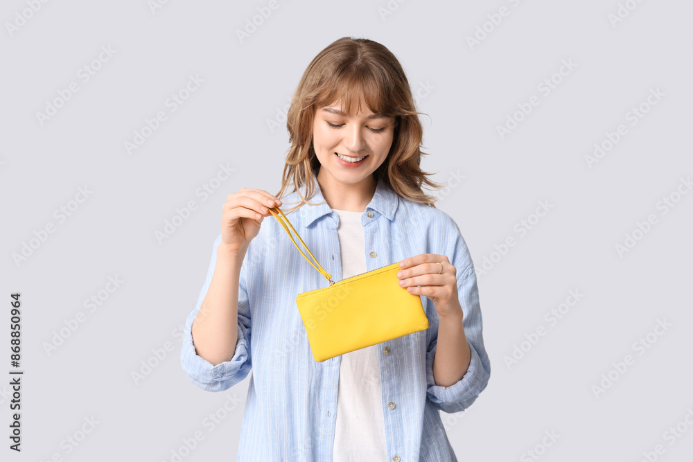 Beautiful young woman holding yellow wallet on grey background Beautiful young woman holding yellow wallet on grey background