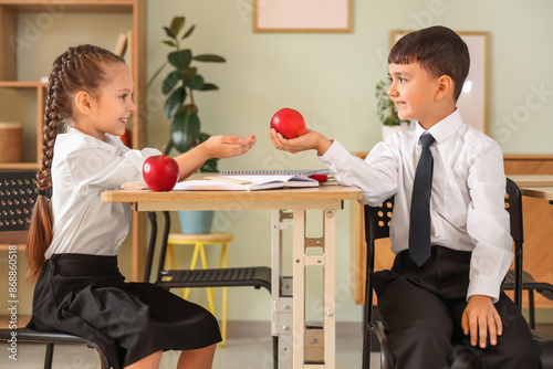 Фотография Little schoolgirl taking apple from classmate in classroom