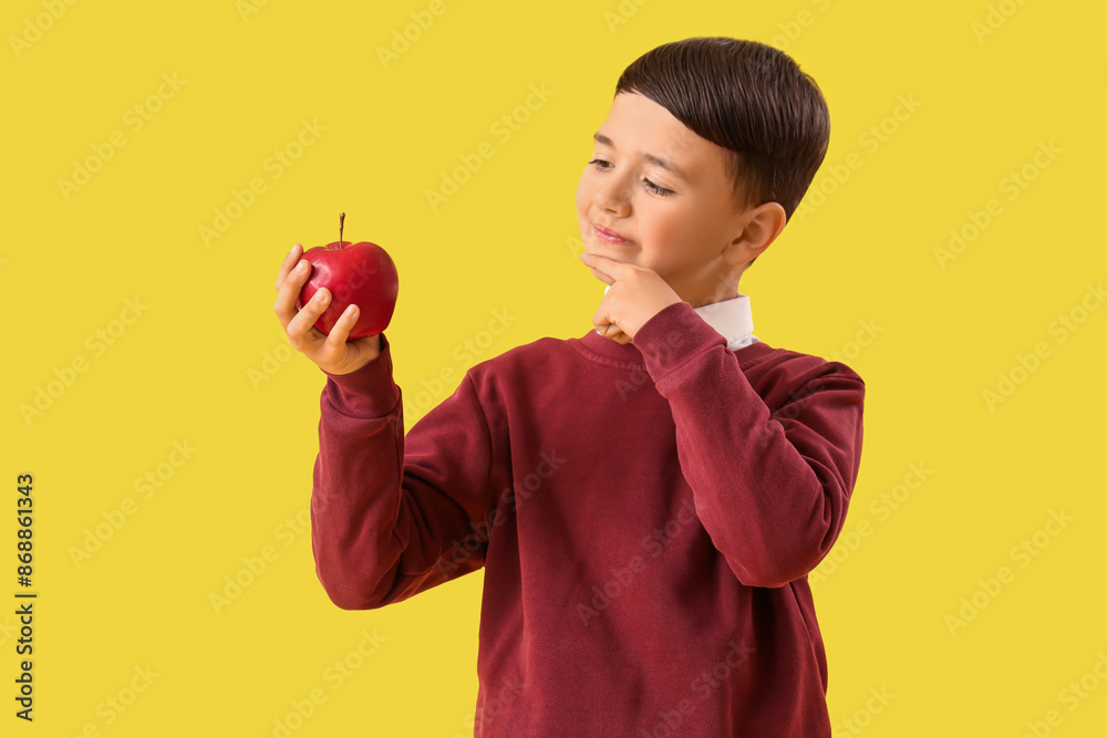 Thoughtful little schoolboy with apple on yellow background Thoughtful little schoolboy with apple on yellow background
