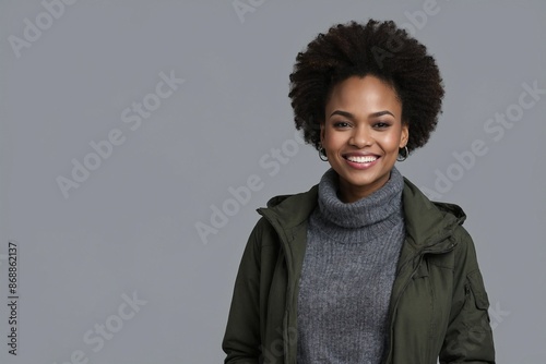 African American woman with smile on her face next to empty space on dark grey background. Beautiful young woman in winter clothes. Space for advertising text.