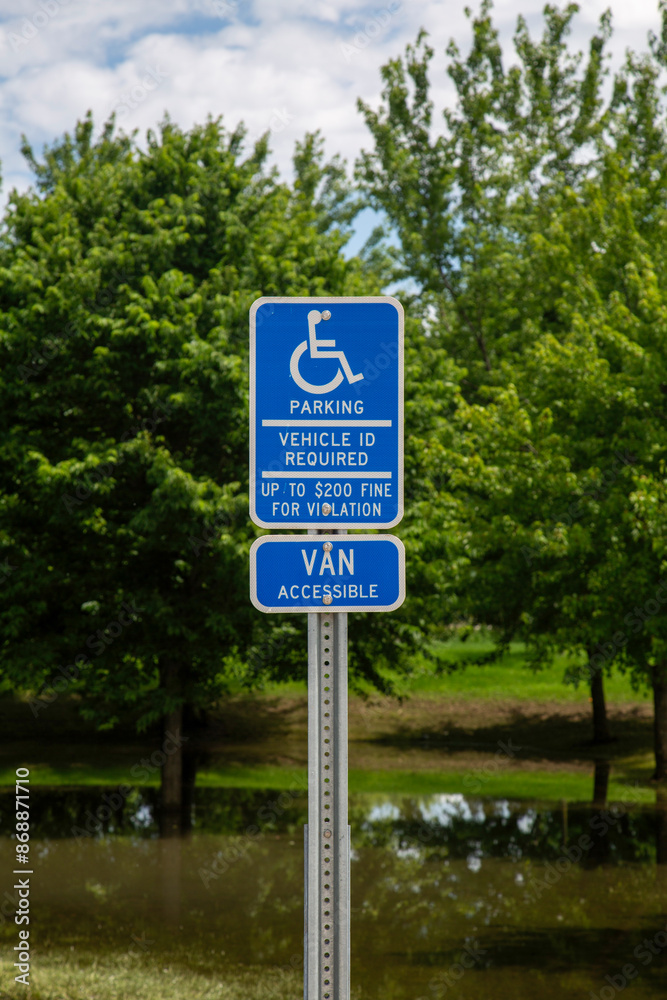 Handicap Parking Sign Closeup Near Park With Trees and Flood Waters Handicap Parking Sign Closeup Near Park With Trees and Flood Waters
