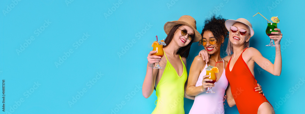 Obraz premium Three multiracial girlfriends wearing swimsuits and sunglasses, laughing and holding colorful cocktails against a blue background. They appear to be having a fun and carefree summer day, copy space