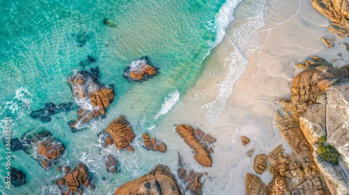 An aerial view featuring turquoise beach waves splashing over rocky formations, offering a vivid portrayal of the interaction between the dynamic sea and steadfast coastal rocks.