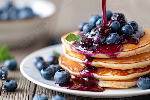 Delicious stack of fluffy pancakes topped with fresh blueberries and drizzled with rich blueberry syrup.