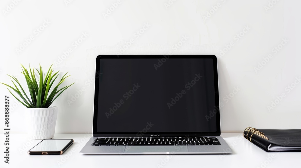 Fototapeta premium Modern laptop computer displaying a blank screen is sitting on a work desk with a smartphone, a plant, and a notebook
