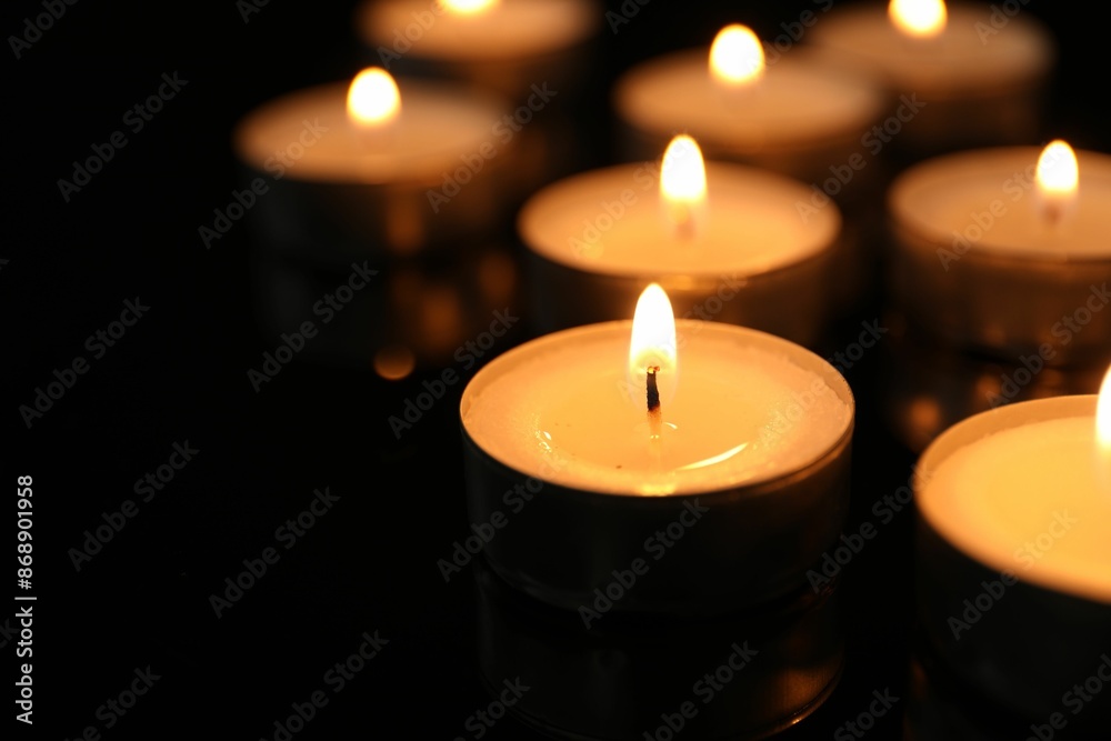 Many burning tealight candles on black background, closeup Many burning tealight candles on black background, closeup