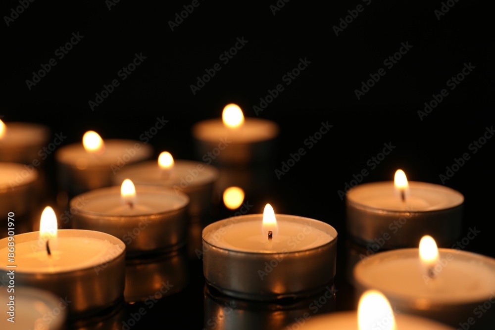 Many burning tealight candles on black background, closeup Many burning tealight candles on black background, closeup