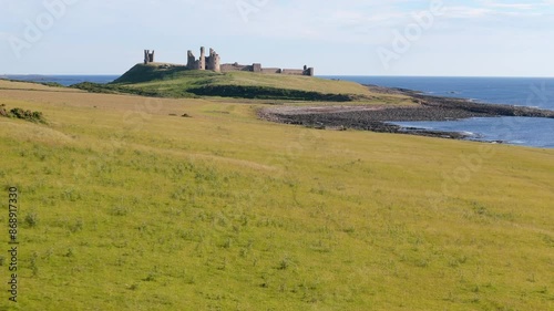 Aerial footage of Dunstanburugh castle ruins on a summer morning with no people photo