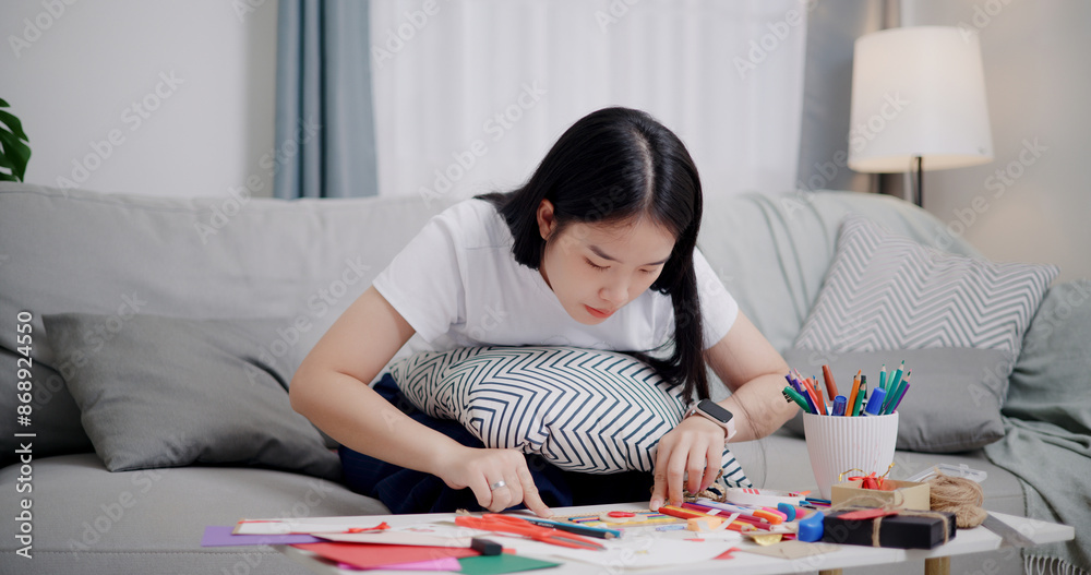High angle view, Young Asian woman sitting on sofa decorating a greeting card in the living room, Holiday hobbies, crafts, DIY cards High angle view, Young Asian woman sitting on sofa decorating a greeting card in the living room, Holiday hobbies, crafts, DIY cards
