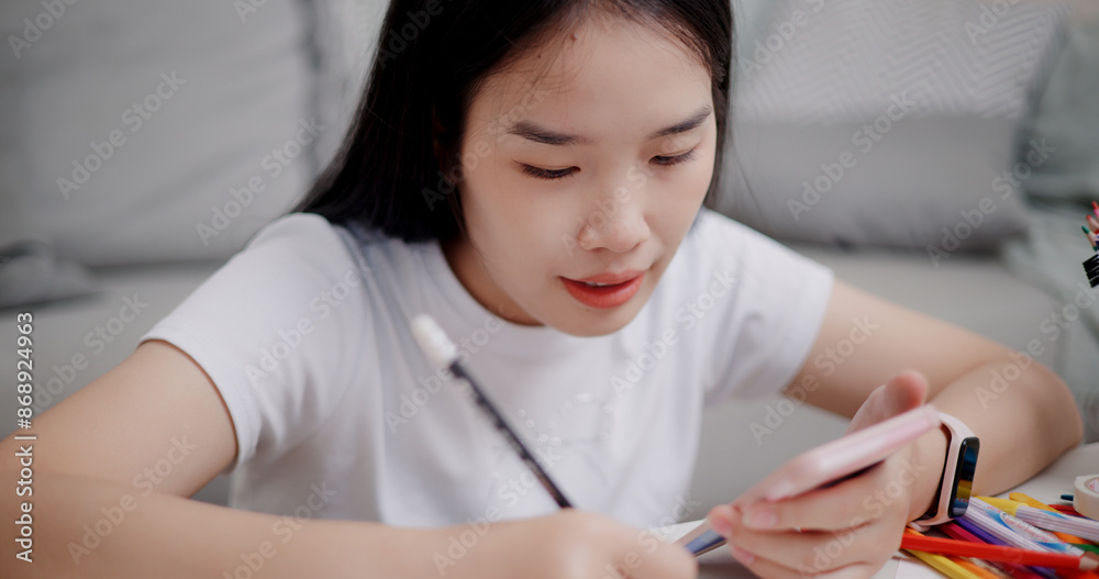 High angle view, Young Asian woman sitting on the floor uses a mobile phone to search for ideas for greeting cards. Holiday hobbies, crafts, DIY cards High angle view, Young Asian woman sitting on the floor uses a mobile phone to search for ideas for greeting cards. Holiday hobbies, crafts, DIY cards