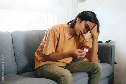 Young Asian Man Touching His Head Suffering From Nosebleed Or Epistaxis And Using Paper Tissue For Stop Bleeding. Healthcare Concept. photo