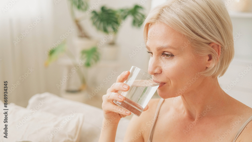 Water balance. Good morning. Healthy habit. Happy woman drinking from glass enjoying hydration in light living room interior at home copy space.