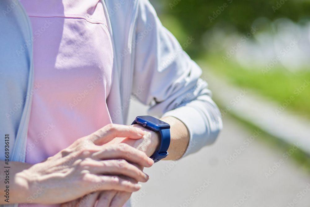 春の新緑の中スマートウォッチで計測をするスポーツウェアをきたシニア女性の手元 春の新緑の中スマートウォッチで計測をするスポーツウェアをきたシニア女性の手元