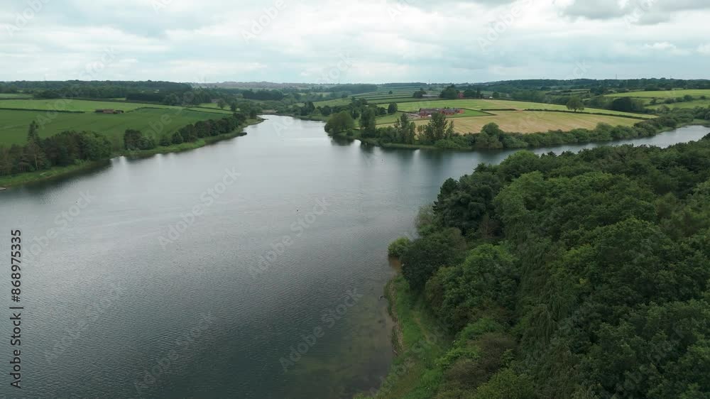Kettering Reservoir is shot from above on a cloudy day. Behind a massive green forest, a beautiful panorama with vivid fields opens up Kettering Reservoir is shot from above on a cloudy day. Behind a massive green forest, a beautiful panorama with vivid fields opens up