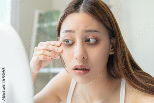 Bored, insomnia asian young woman, girl looking at mirror hand touching under eyes with problem of black circles or panda puffy, swollen and wrinkle on face. Sleepless, sleepy healthcare person.