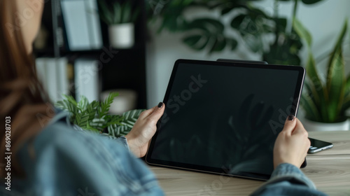 girl's hands are holding a an ipad tablet with a black screen at the wooden desk