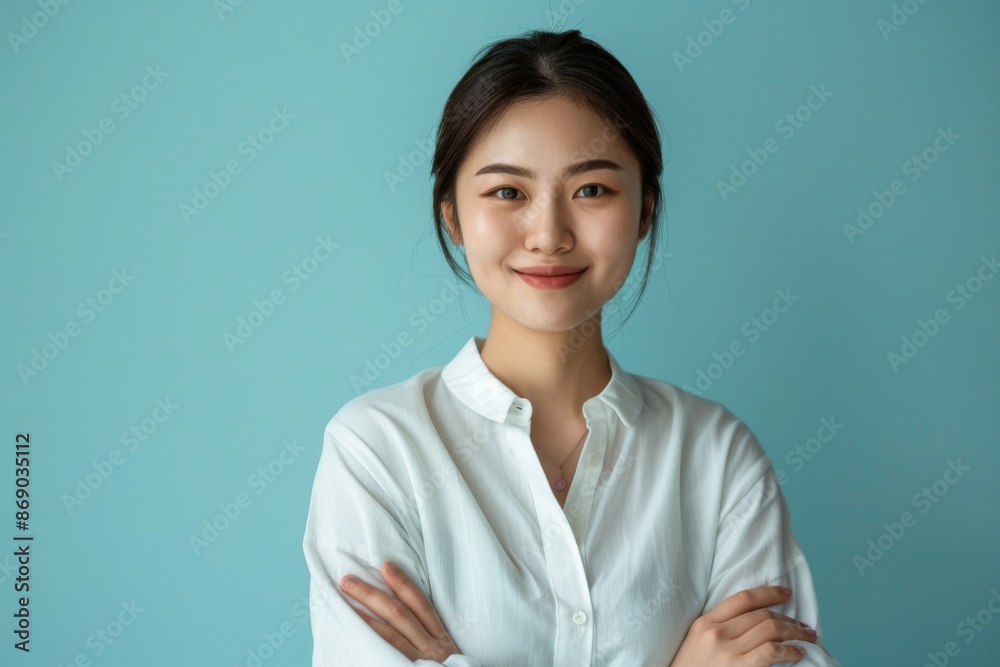confident smiling young asian woman with crossed arms on light blue background confident smiling young asian woman with crossed arms on light blue background