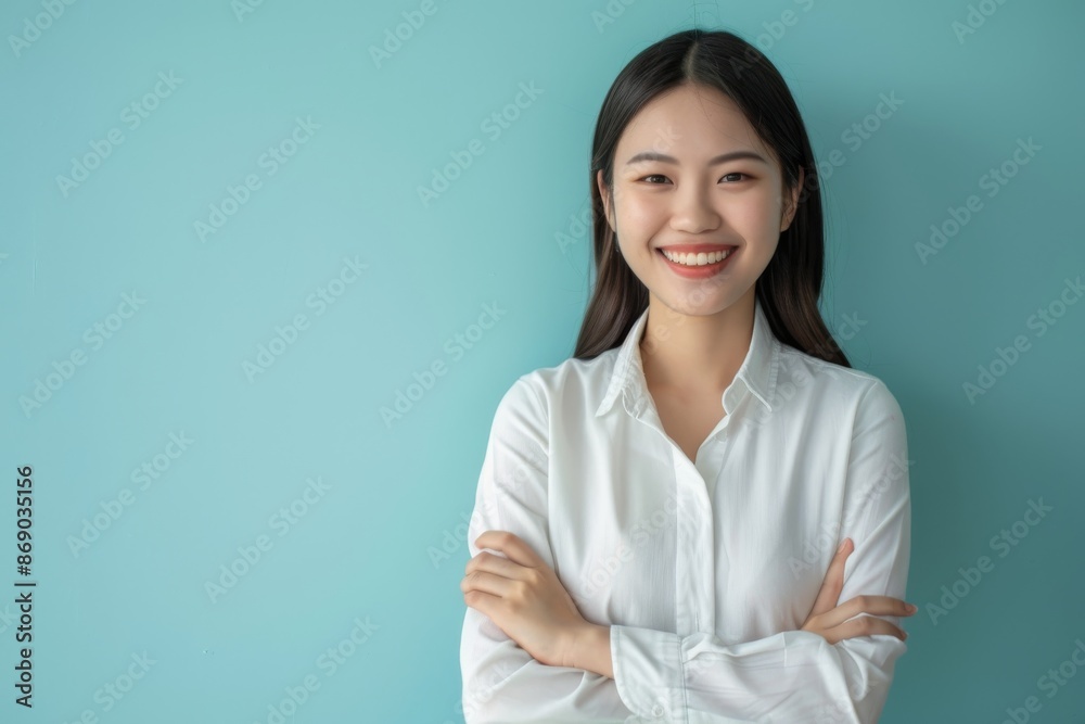 confident smiling young asian woman with crossed arms on light blue background confident smiling young asian woman with crossed arms on light blue background