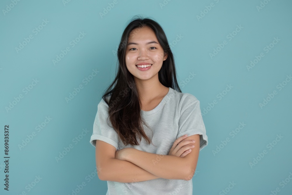 confident smiling young asian woman with crossed arms on light blue background confident smiling young asian woman with crossed arms on light blue background