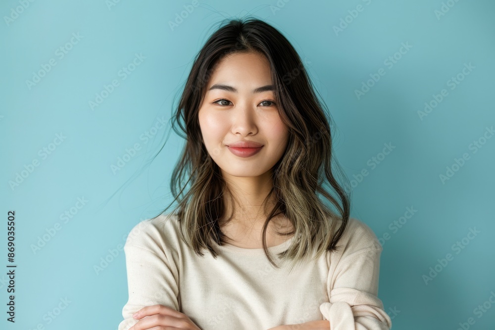 confident smiling young asian woman with crossed arms on light blue background confident smiling young asian woman with crossed arms on light blue background