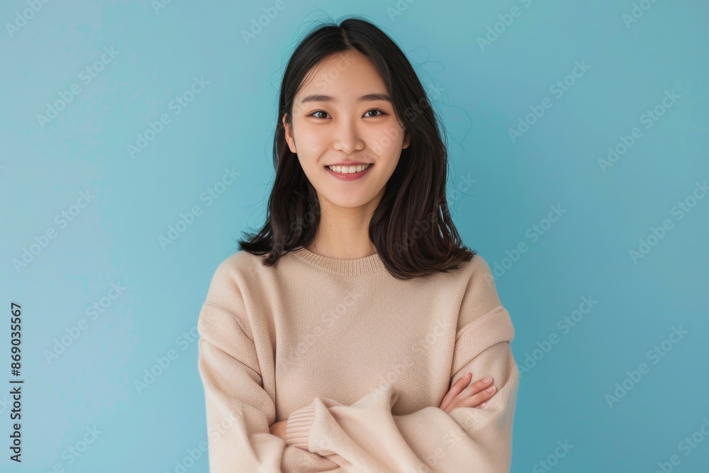 confident smiling young asian woman with crossed arms on light blue background confident smiling young asian woman with crossed arms on light blue background