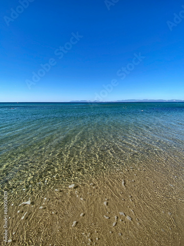 The beach of luxury hotel. Sunny day, calm waveless sea, blue sky. Soft yellow-gold brown-gold sand shines on beach. sea ​​waves hitting the seashore. clear and clean sea water. Balıkesir in Turkiye photo