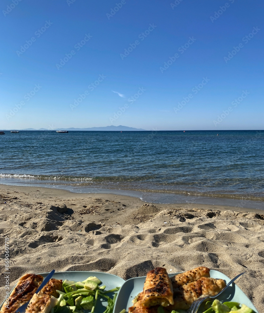 Obraz premium Luxury hotel's beach food snack plates. Sunny day, calm waveless sea, blue sky. Soft brown-gold sand shines on the beach. sea ​​waves hitting the seashore. clear, clean sea water. Balıkesir in Turkiye