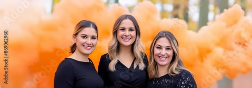 Three women are posing for a photo in front of a large orange cloud of smoke. Scene is playful and fun, as the women are smiling and enjoying themselves. The orange smoke adds a sense of excitement