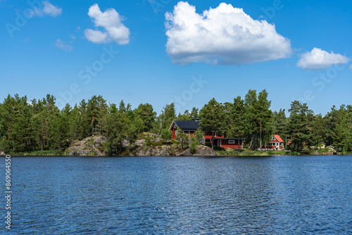 Beautiful panoramic view of the lake or the bay of the Baltic Sea. The rocky shores are covered with forests pines, spruces, firs, coniferous trees. Typical Scandinavian wooden red house on the coast.