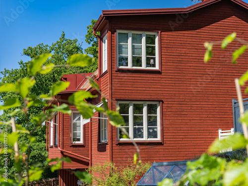 Country beautiful view. Wall of a wooden house with large windows. Old house villa cottage painted in brown-red color. Greenhouse in the yard.