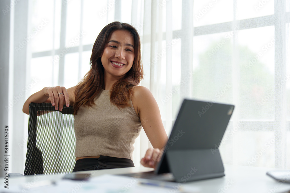 Confident Asian businesswoman, independent business owner sitting in a chair at a desk A smiling face uses a laptop to work and analyze financial report documents. office investment. Confident Asian businesswoman, independent business owner sitting in a chair at a desk A smiling face uses a laptop to work and analyze financial report documents. office investment.