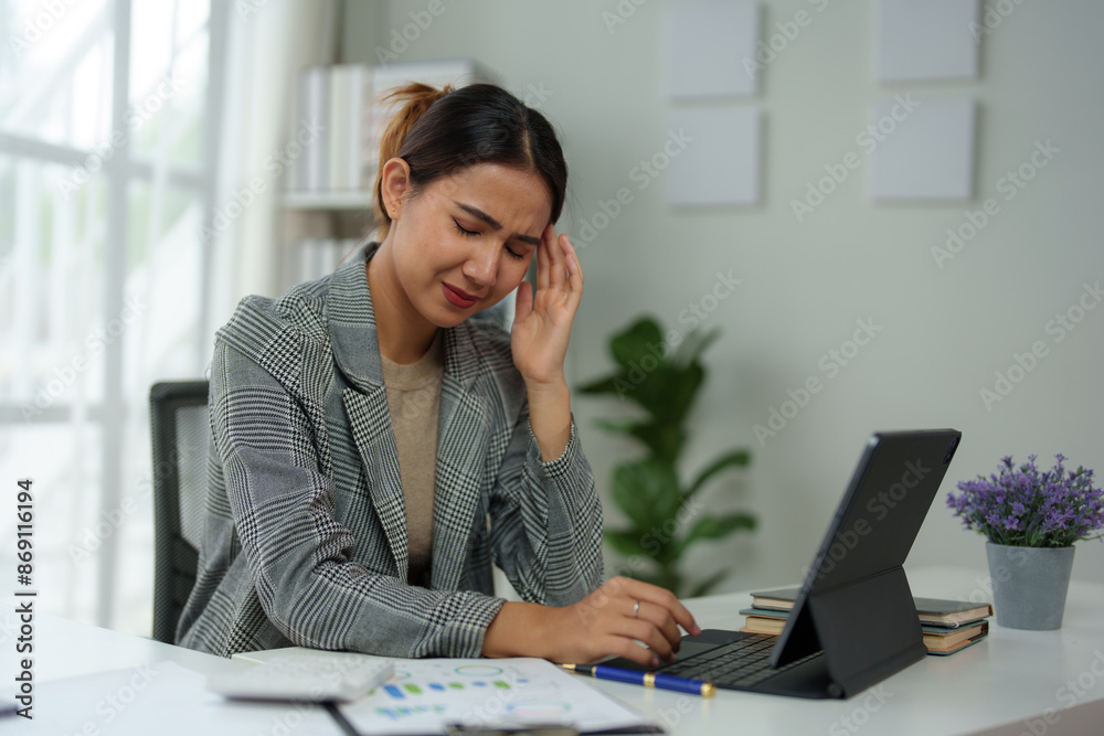 Asian woman, independent businesswoman, feeling stressed, achy, and sleepy while working on a laptop. Tired Asian businesswoman has a headache at the office Feeling sick at work. Asian woman, independent businesswoman, feeling stressed, achy, and sleepy while working on a laptop. Tired Asian businesswoman has a headache at the office Feeling sick at work.