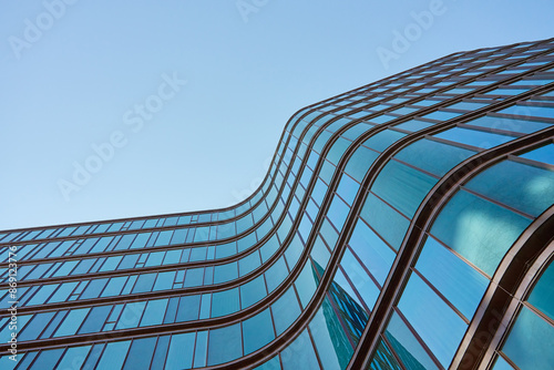 Obraz na płótnie Modern building with curved glass facade reflecting sky. Contemporary architectural design against a clear blue backdrop w salonie