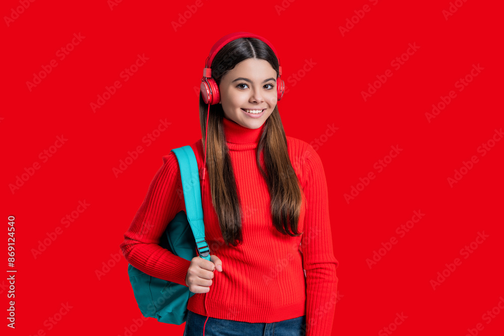 Teen student girl with school backpack has online education in headphones isolated on red Teen student girl with school backpack has online education in headphones isolated on red
